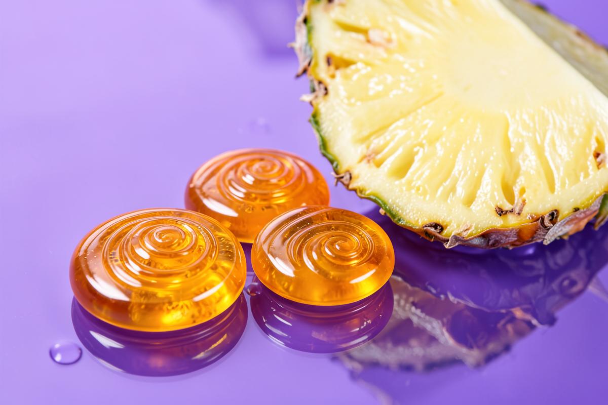 Pineapple and spiral-shaped gummies on a glossy lavender surface